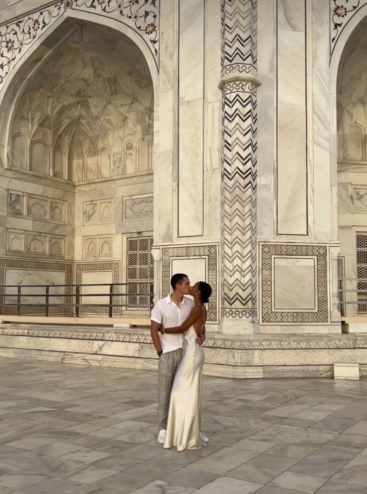 a man and woman standing next to each other in front of a building with arches