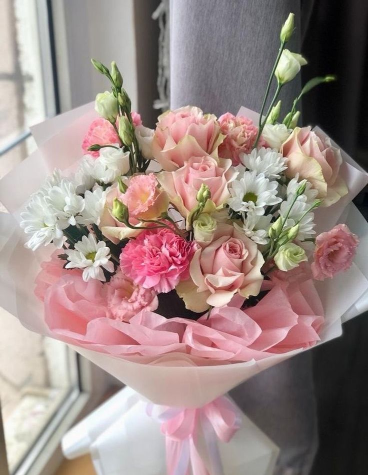 a bouquet of pink and white flowers in front of a window with a person standing next to it