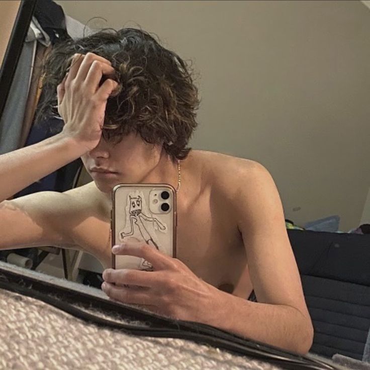 a shirtless man looking at his cell phone while sitting in front of a mirror