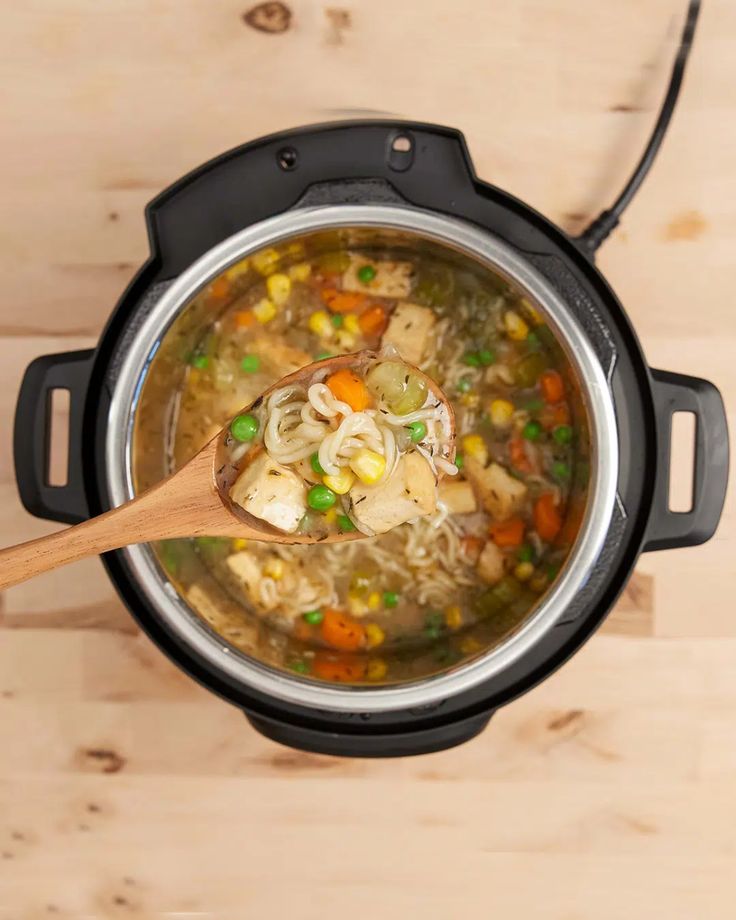 an overhead view of a pot of soup with a wooden spoon in it, on a wood table