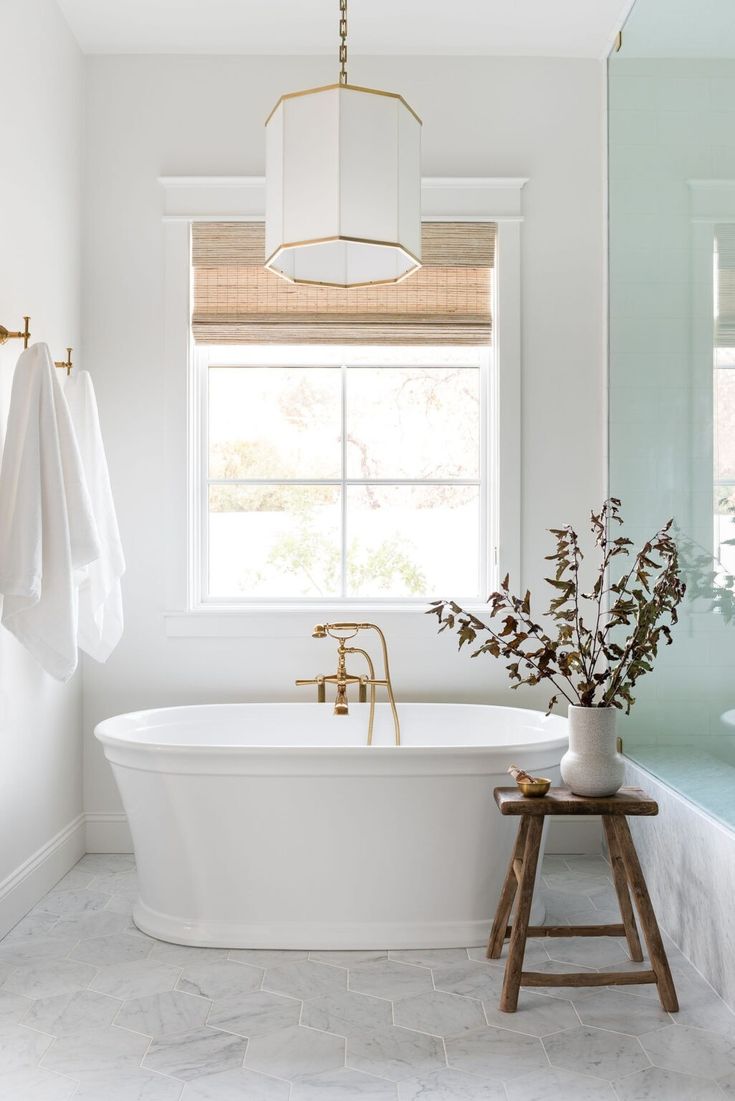 a white bath tub sitting under a window next to a wooden step stool and vase with flowers