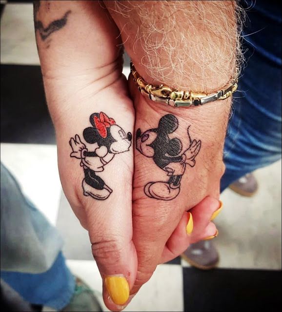 two people holding hands with mickey and minnie mouse tattoos on their fingers, one has a red bow in her hair