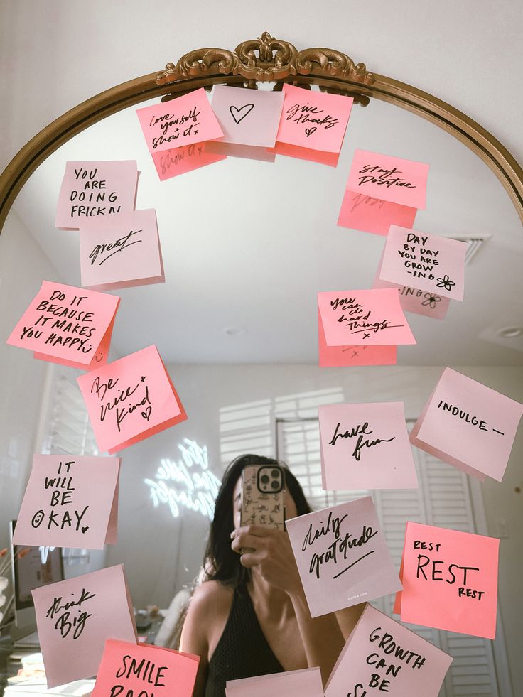 a woman taking a selfie in front of a mirror with sticky notes on it