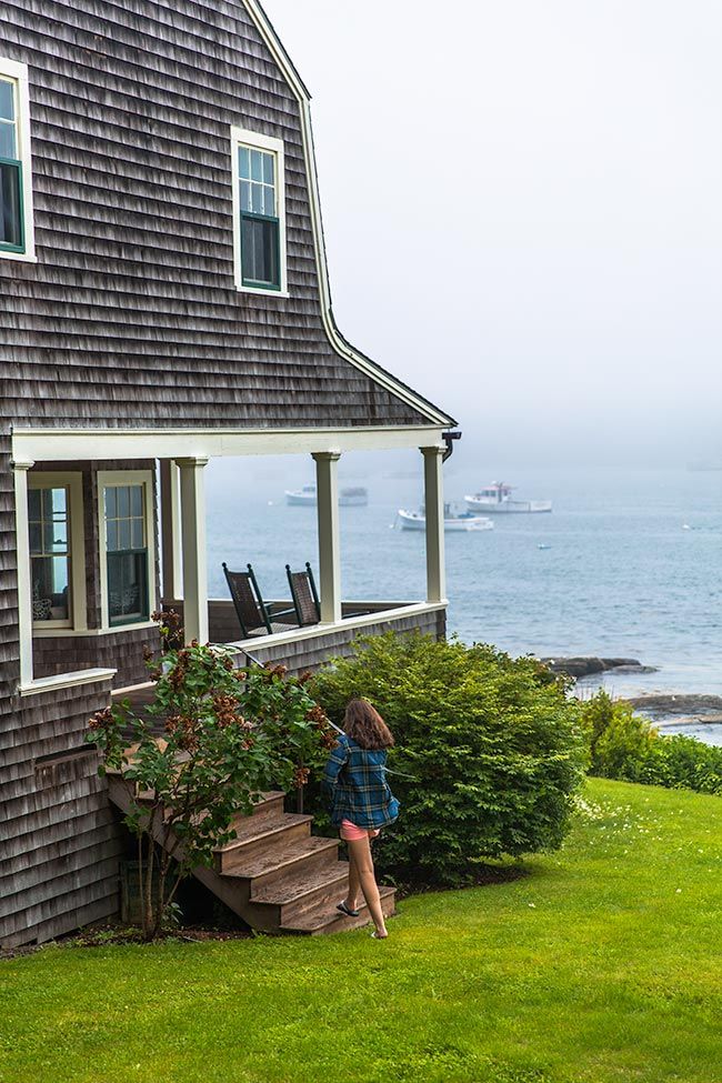 a woman sitting on steps in front of a house next to the ocean and boats