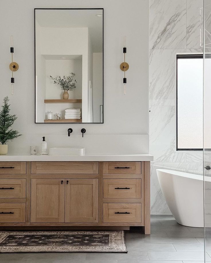 a white bath tub sitting next to a wooden sink vanity under a large framed mirror