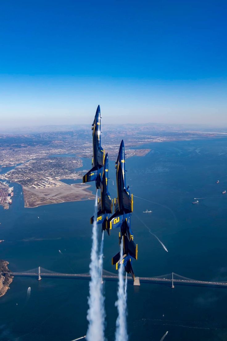 two blue and yellow jets flying over the ocean