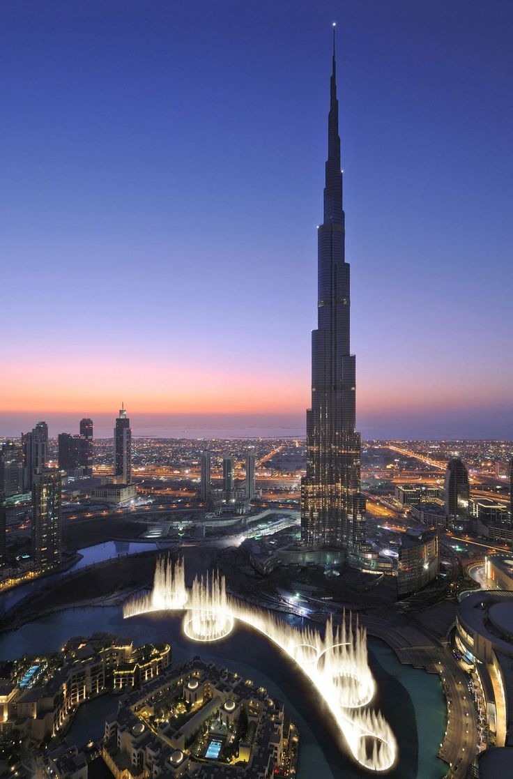 the burj tower towering over the city at night, with water fountains in front