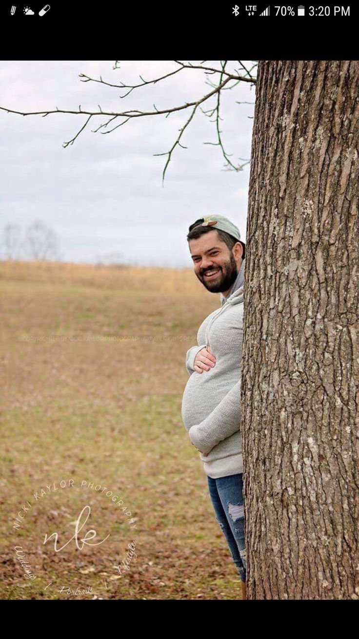 a man standing next to a tree with his arms wrapped around the tree's trunk