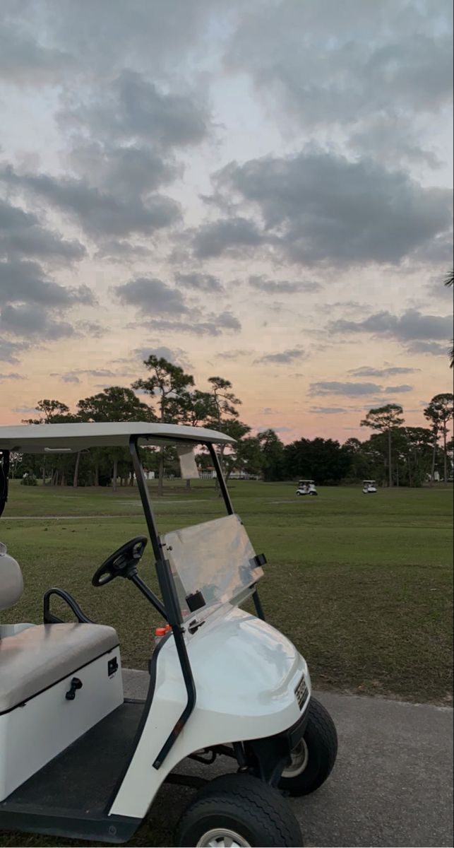 a white golf cart parked on the side of a road near a field at sunset