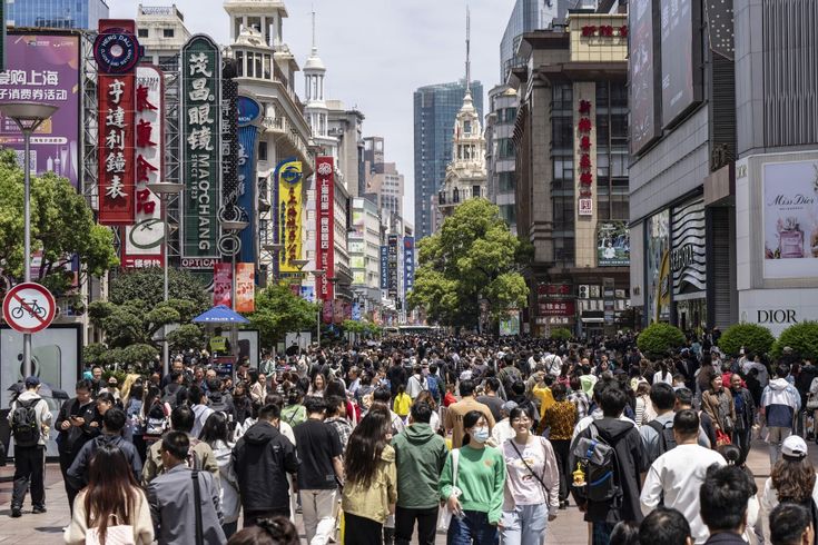 a crowd of people walking down a street next to tall buildings with signs on them