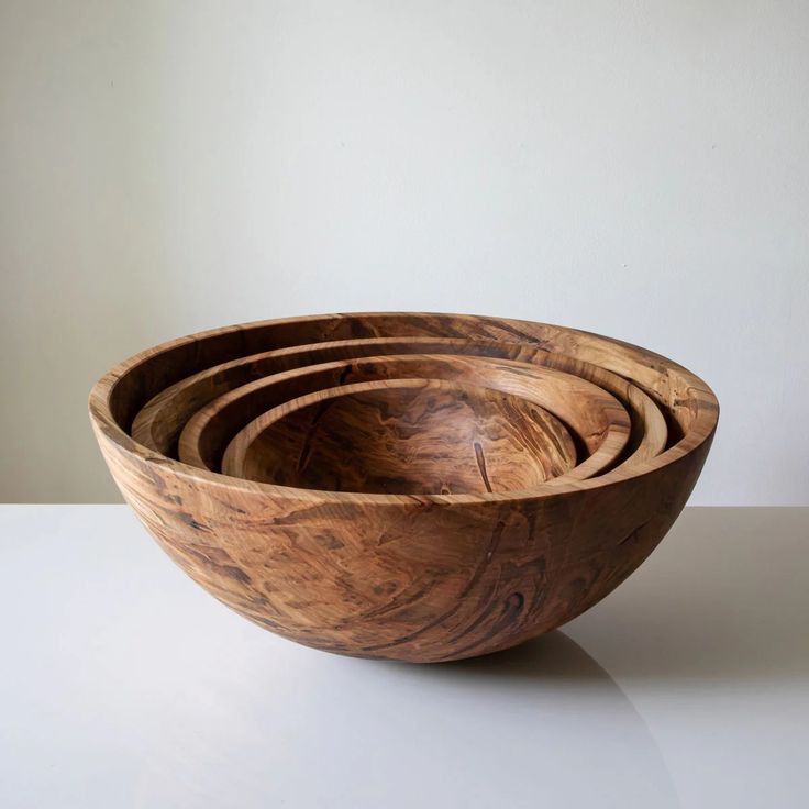 four wooden bowls stacked on top of each other in front of a plain white wall