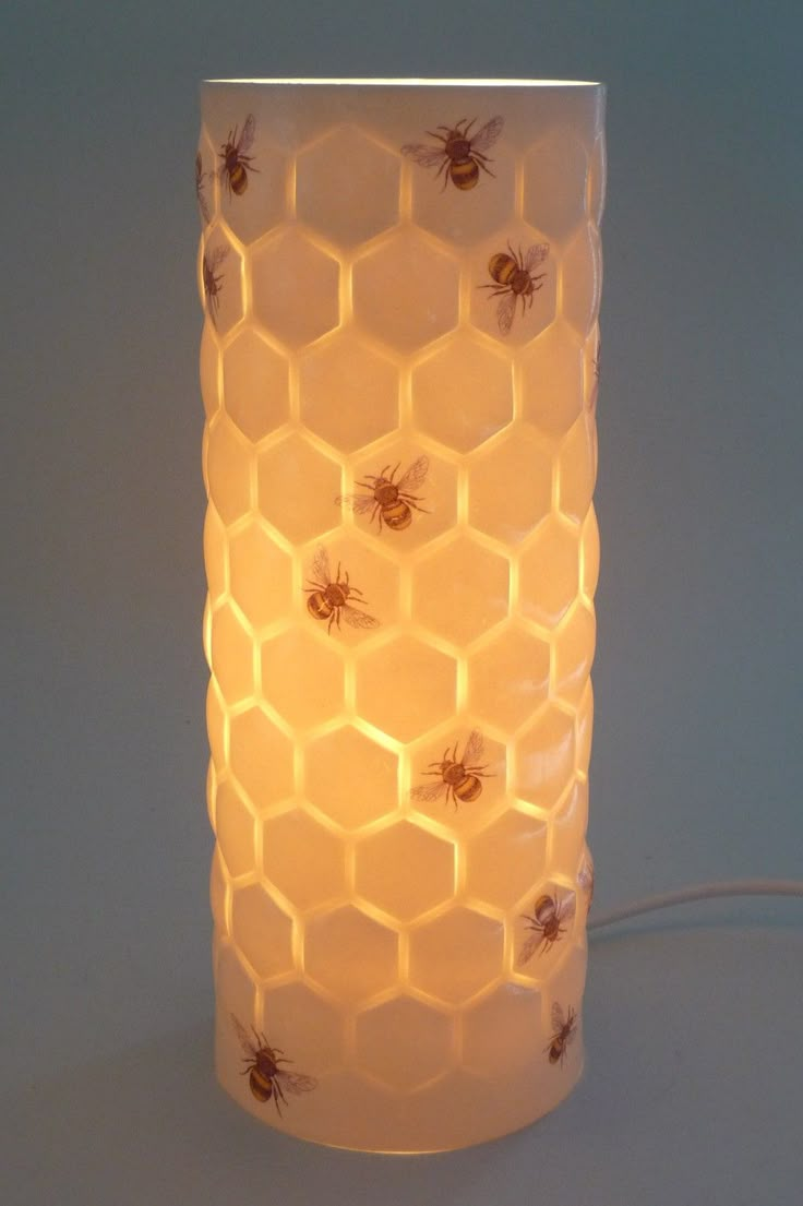 a white vase with honeycombs on it sitting next to a corded light