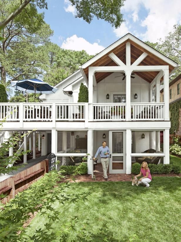 two people sitting on the grass in front of a large white house with porches and balconies