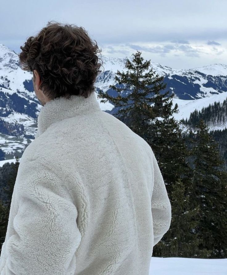 a person standing on top of a snow covered slope looking at the mountains in the distance