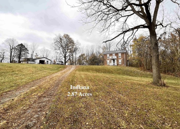 an empty dirt road in front of a large house with trees on the other side