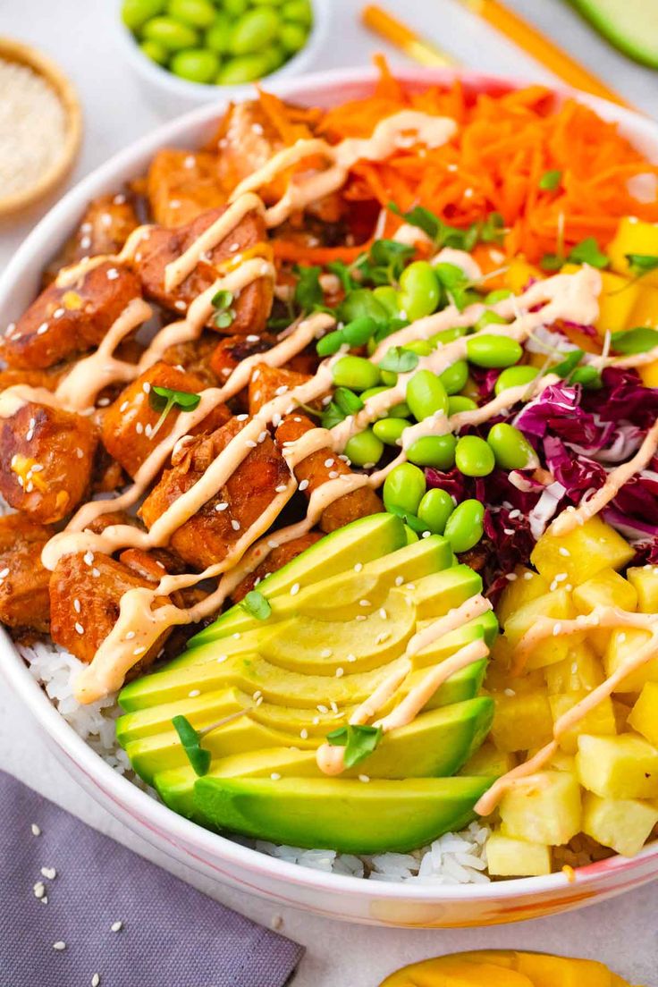 a bowl filled with meat, vegetables and rice next to sliced avocado on a table