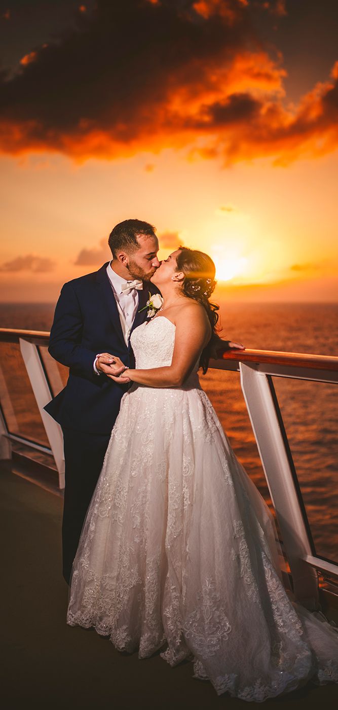 a bride and groom kissing on the deck of a cruise ship at sunset with the sun setting behind them