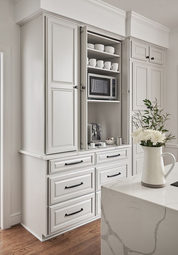 a kitchen with white cabinets and marble counter tops in the center, along with a vase filled with flowers