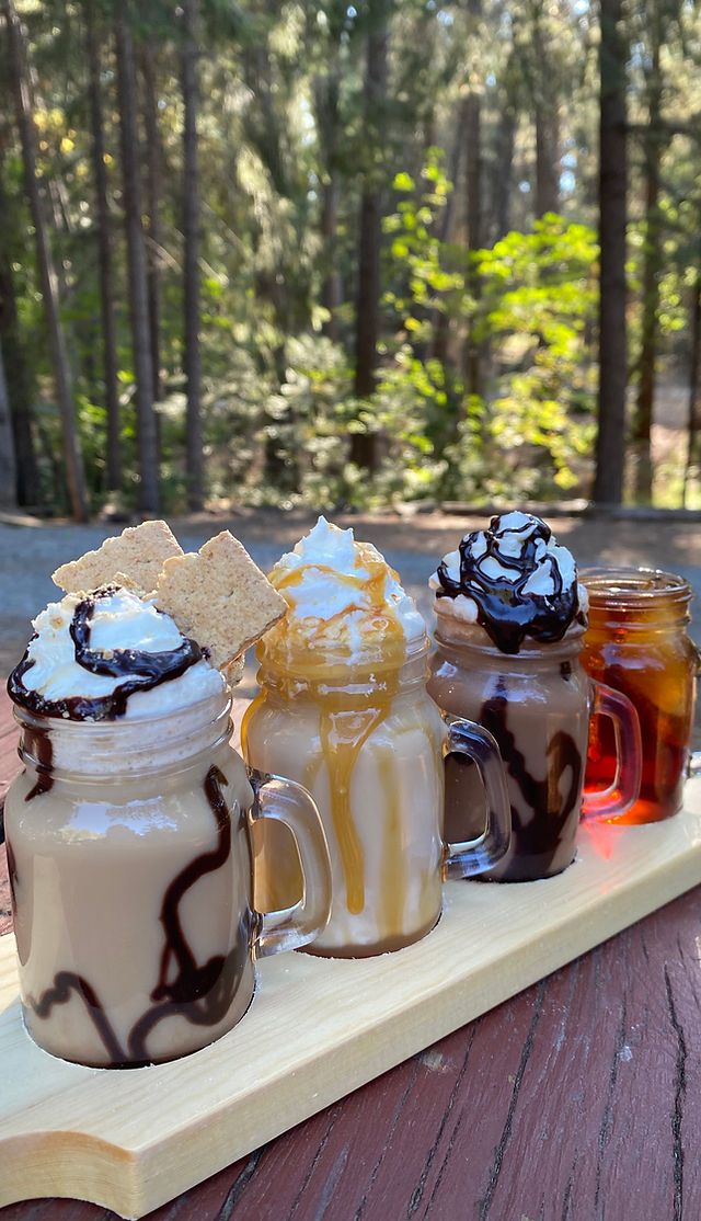 four different kinds of drinks on a wooden tray with trees in the backgroud