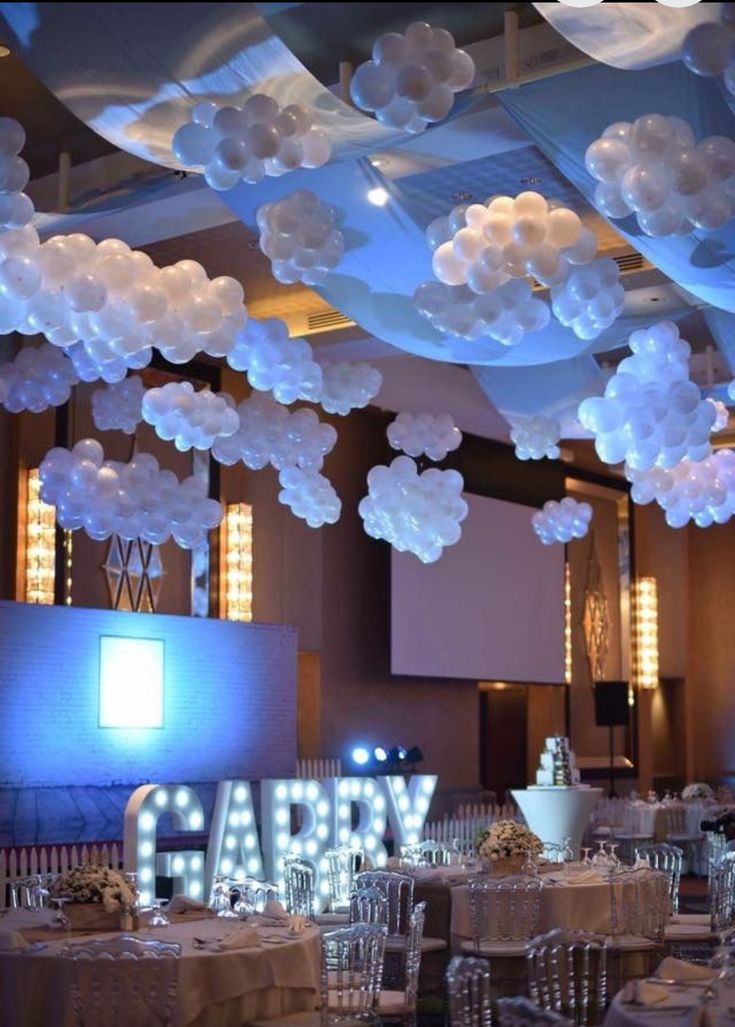 a large room filled with lots of tables covered in white frosted paper flowers and balloons