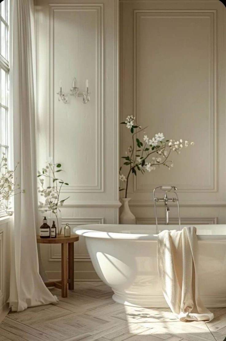 a white bath tub sitting under a window next to a vase with flowers in it