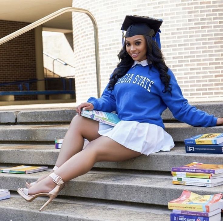 a woman sitting on steps with books in front of her and wearing a graduation cap