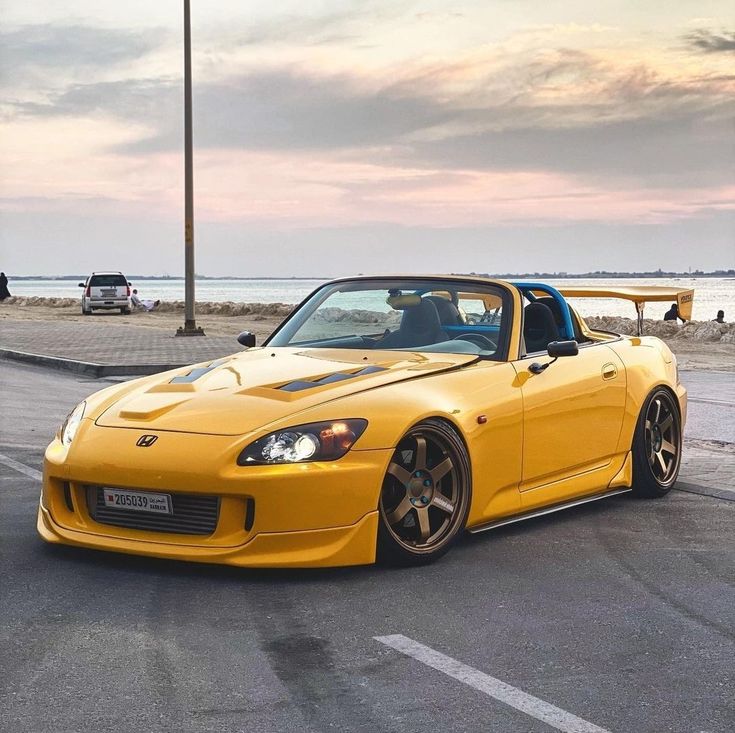 the yellow sports car is parked on the side of the road next to the ocean