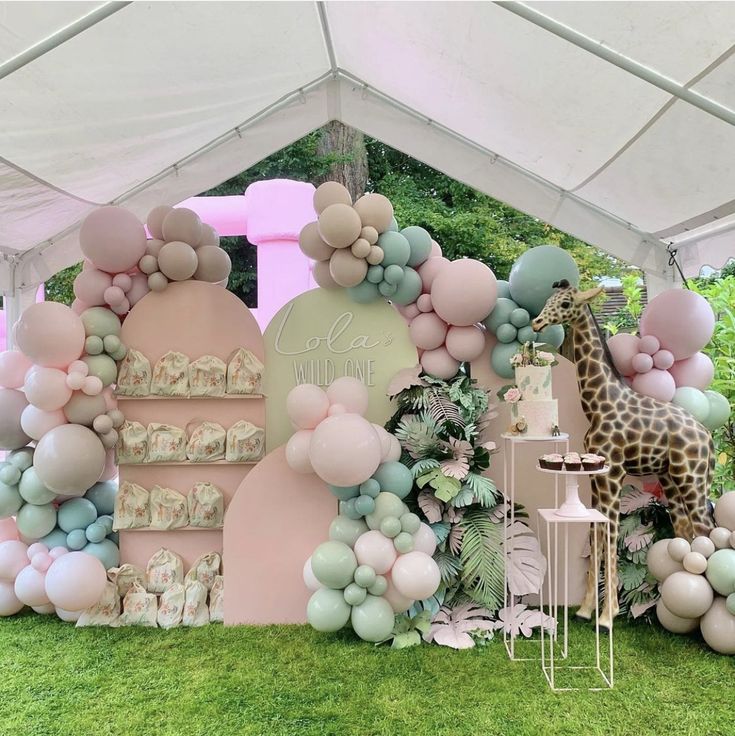 a giraffe is standing in front of a backdrop made out of balloons and other items