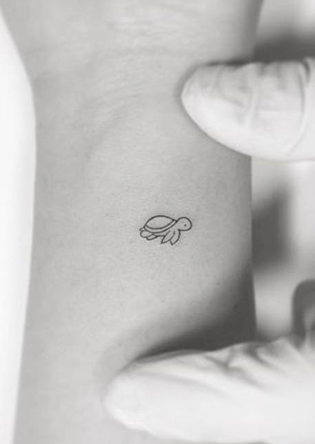 a small turtle tattoo on the back of a woman's left arm and wrist