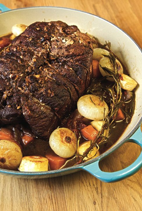 a pot roast with potatoes and carrots on a wooden table