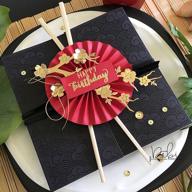 a black and red birthday card with gold foil flowers on it, sitting on top of a white plate