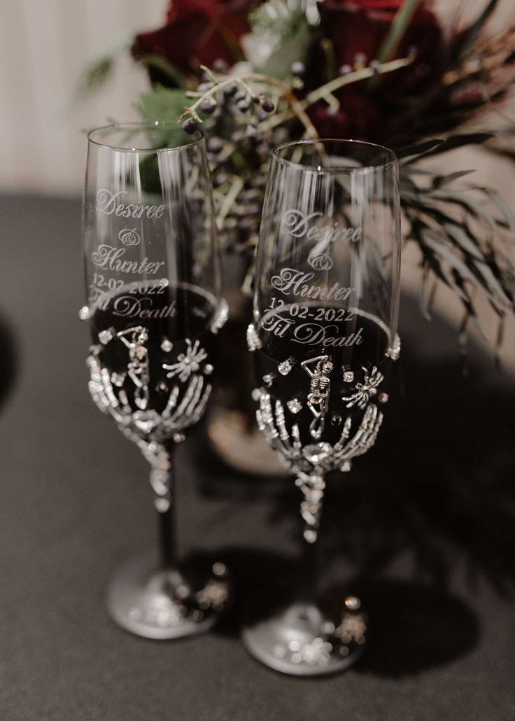 two wine glasses sitting on top of a table next to a vase filled with flowers