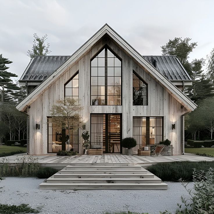 This image showcases a stunning split-level Scandinavian-style home featuring a classic gabled roof and modern design. The exterior is clad in weathered wood siding, complemented by large, floor-to-ceiling windows that flood the interior with natural light. A spacious wooden deck with steps leads to the entrance, surrounded by neatly maintained plants and minimalist outdoor furniture. This home combines rustic charm with contemporary elegance, nestled in a serene, forested landscape. Window Model Architecture, Twin Gable House Exterior, Two Peak House Exterior, Front Porch With Gable, Modern Scandinavian Architecture, Split Level Barndominium, Wooden Houses Exterior, Scandinavian Style Home Exterior, Nordic Cottage Exterior