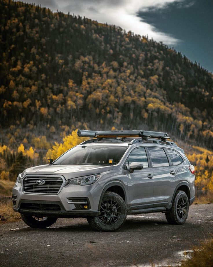 a silver subarunt parked on the side of a road with mountains in the background