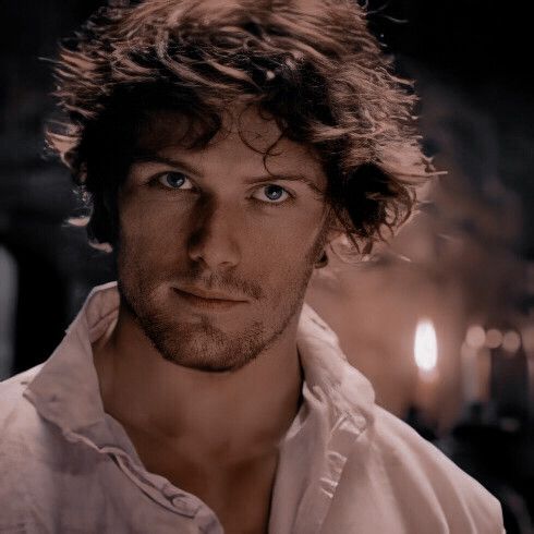 a man with curly hair and blue eyes looks at the camera while wearing a white shirt