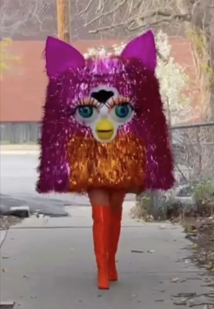 a woman walking down a sidewalk wearing a purple and orange furry cat costume on top of her head