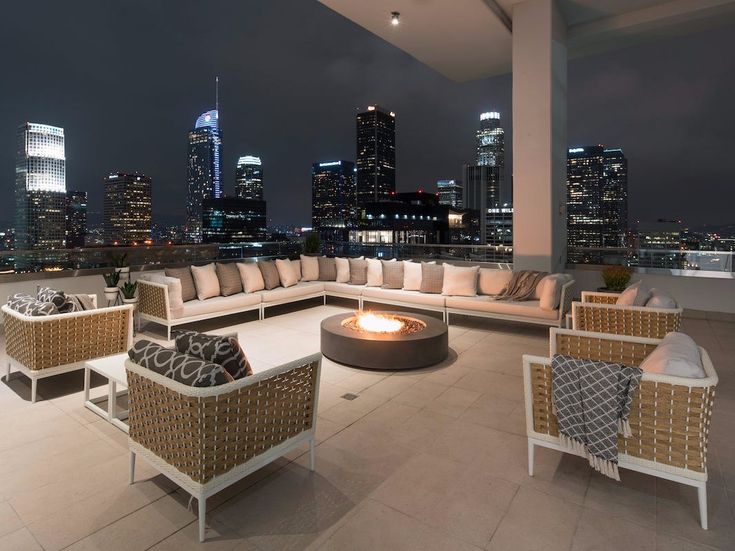 an outdoor living area with wicker furniture and cityscape in the background at night