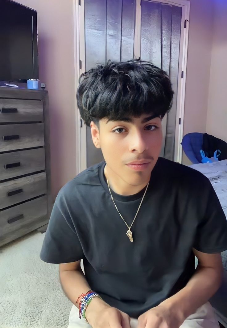 a young man sitting on top of a bed next to a dresser