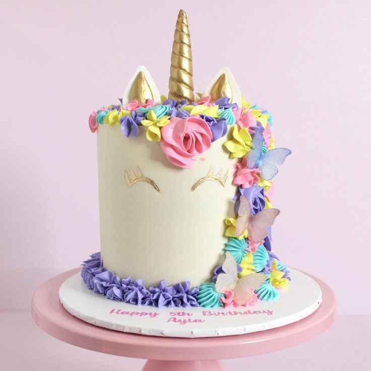 a birthday cake decorated with flowers and a unicorn's head on a pink pedestal