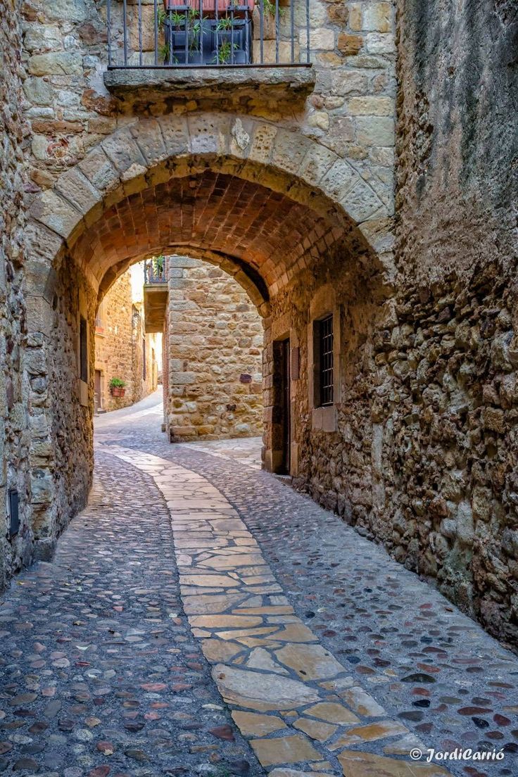 an alley way with stone walls and cobblestone walkway leading up to a balcony