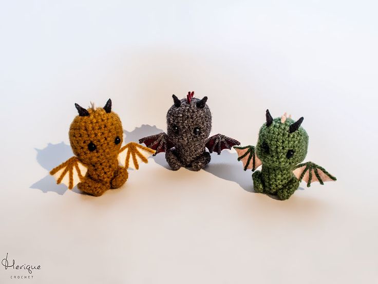 three crocheted dragon figurines sitting next to each other on a white surface