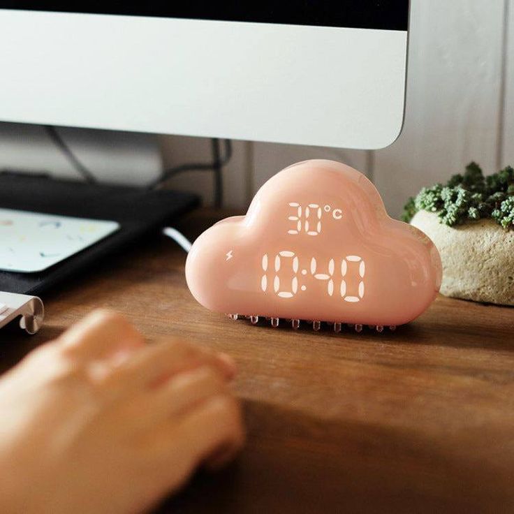 a pink alarm clock sitting on top of a wooden desk next to a computer monitor