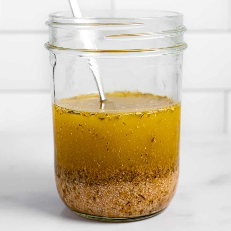 a glass jar filled with yellow liquid on top of a white counter next to a wooden spoon