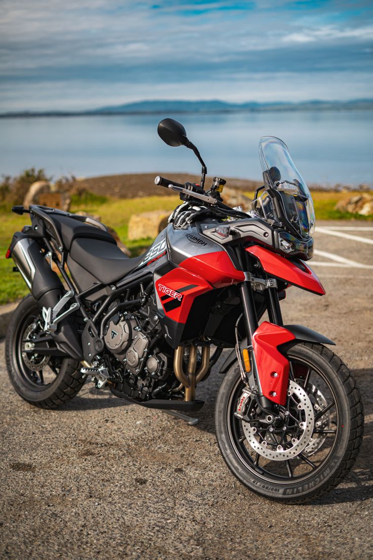 a red and black motorcycle parked on top of a parking lot next to the ocean