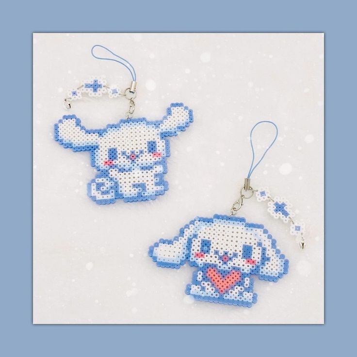 two cross stitch keychains that are shaped like animals with hearts in their paws