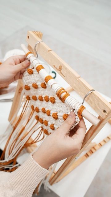 two hands are working on an old weaving loom with orange beads and white yarn