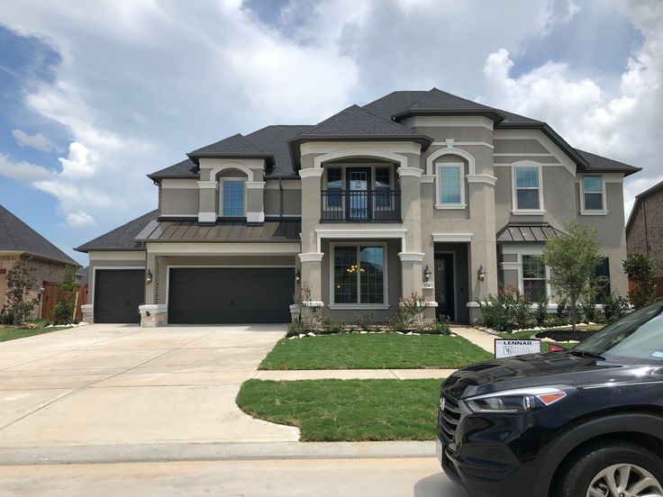 a car is parked in front of a large house with two garages on both sides