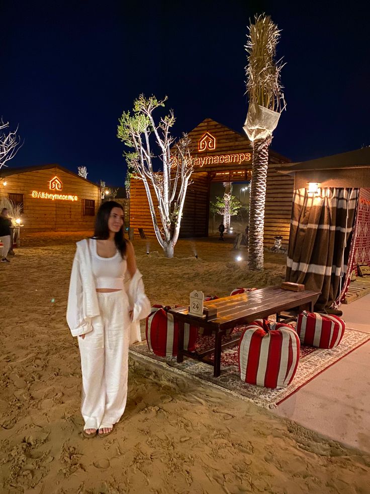 a woman standing in the sand near a table