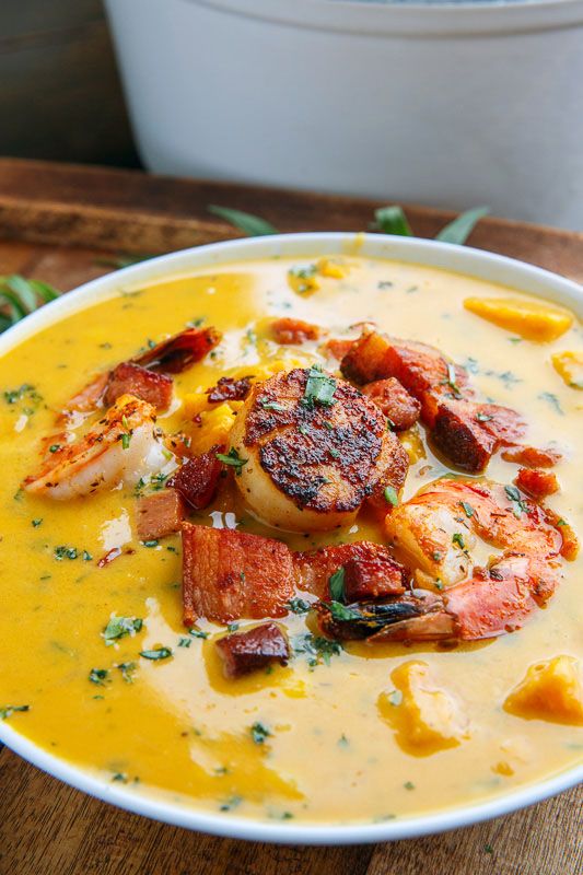 a bowl of soup with shrimp and grits in it on a wooden table next to a spoon