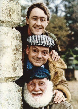 two men with beards and hats leaning against a brick wall, one holding on to another man's shoulder